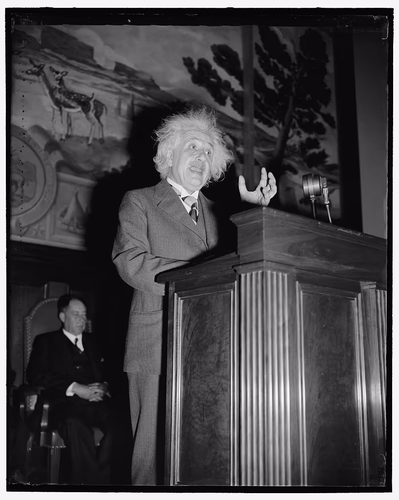 Albert Einstein speaking energetically from a wooden lectern in 1934